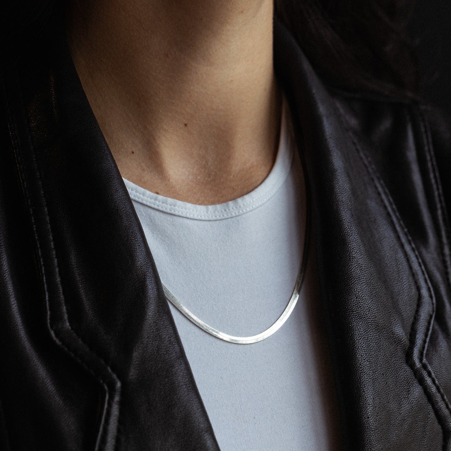 Silver herringbone chain necklace worn around person's neck over white shirt.