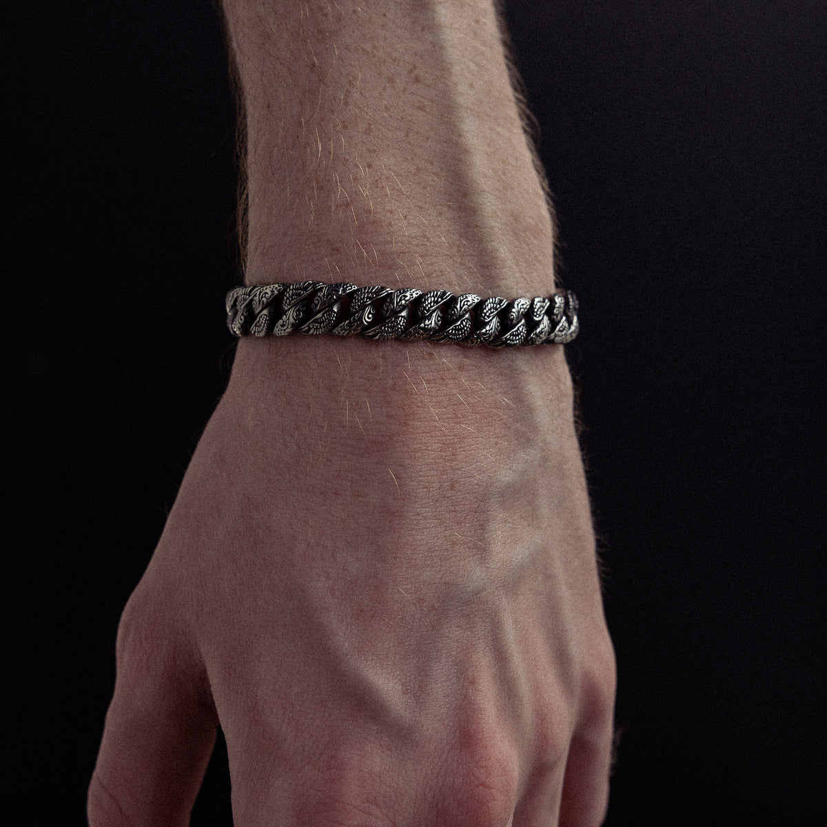 Silver-tone twisted chain bracelet worn on wrist against black background.
