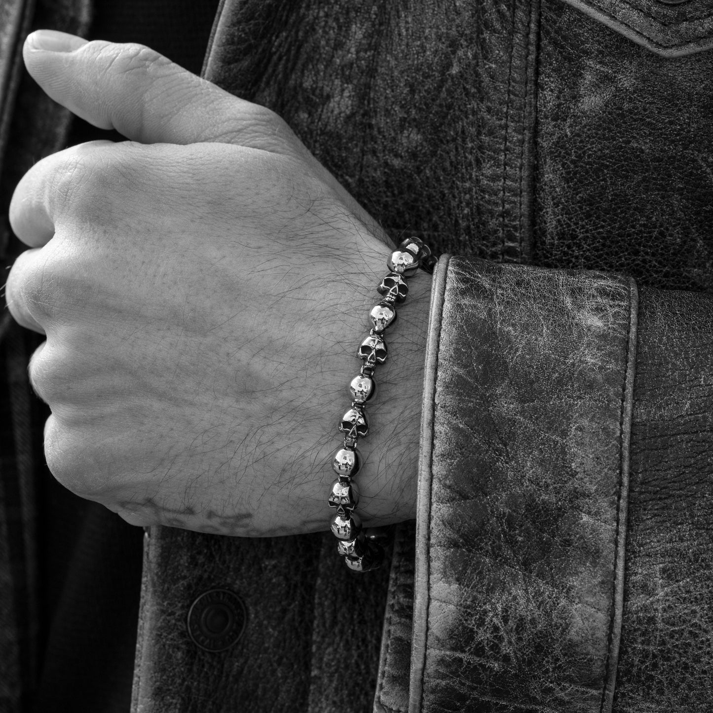 Close-up of a hand wearing a skull-themed bracelet on a dark background