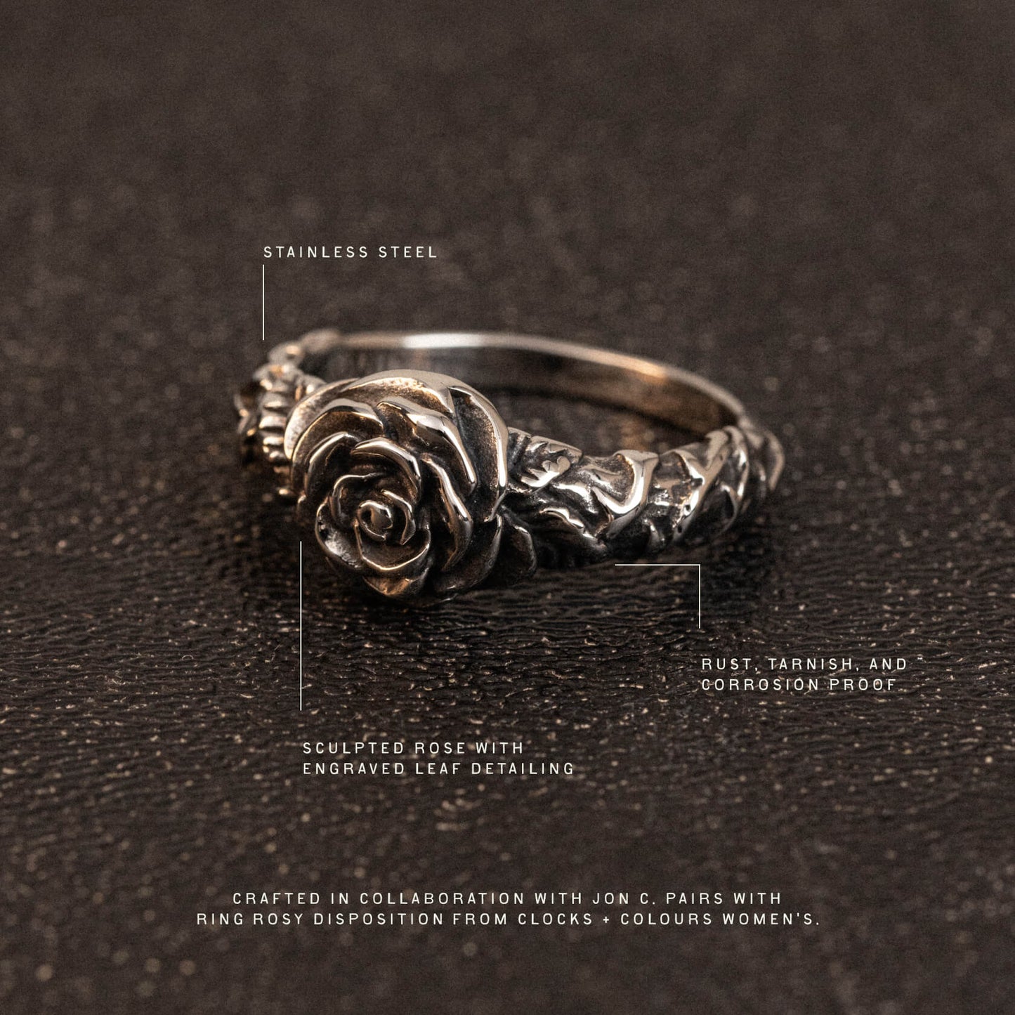 Stainless steel ring featuring a sculpted rose with engraved leaf detailing on the band, displayed on dark textured surface.