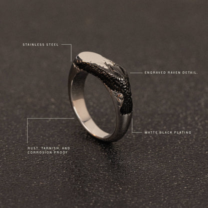 Black stainless steel ring with engraved raven head detail and matte black plating on textured surface.