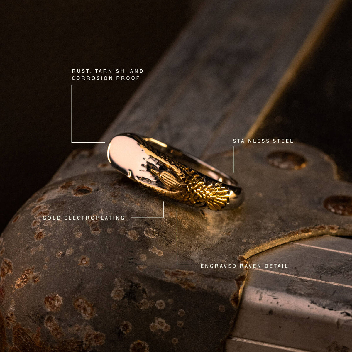 Gold-plated stainless steel ring with engraved raven detail, displayed on rustic metal surface.