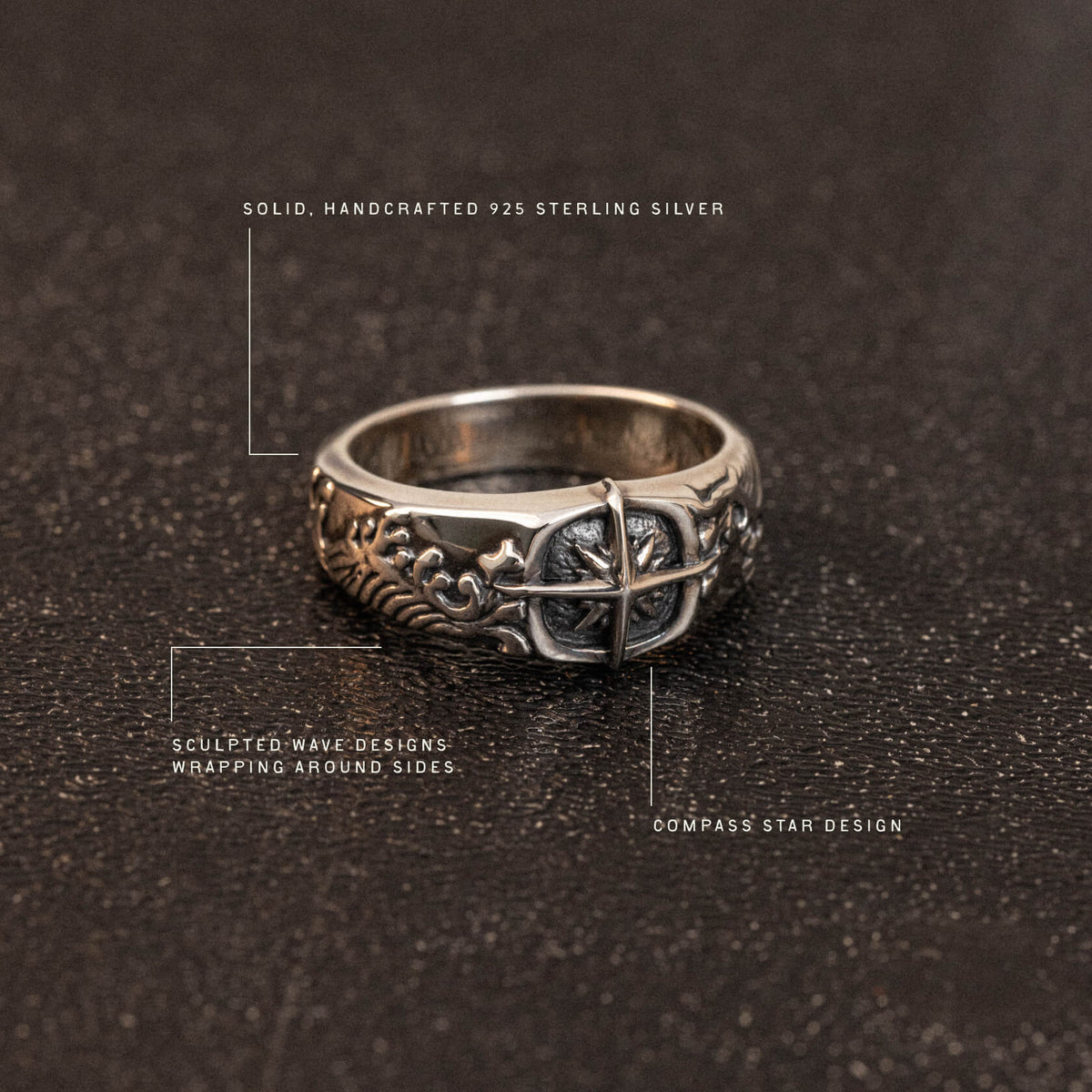 Sterling silver band ring with sculpted wave patterns and compass star motif on dark textured surface.