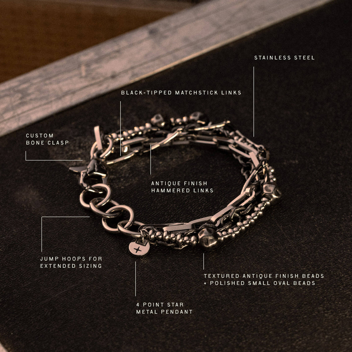 Antique finish metal bracelet with hammered links, textured beads, matchstick accents, bone clasp, and star pendant on dark b