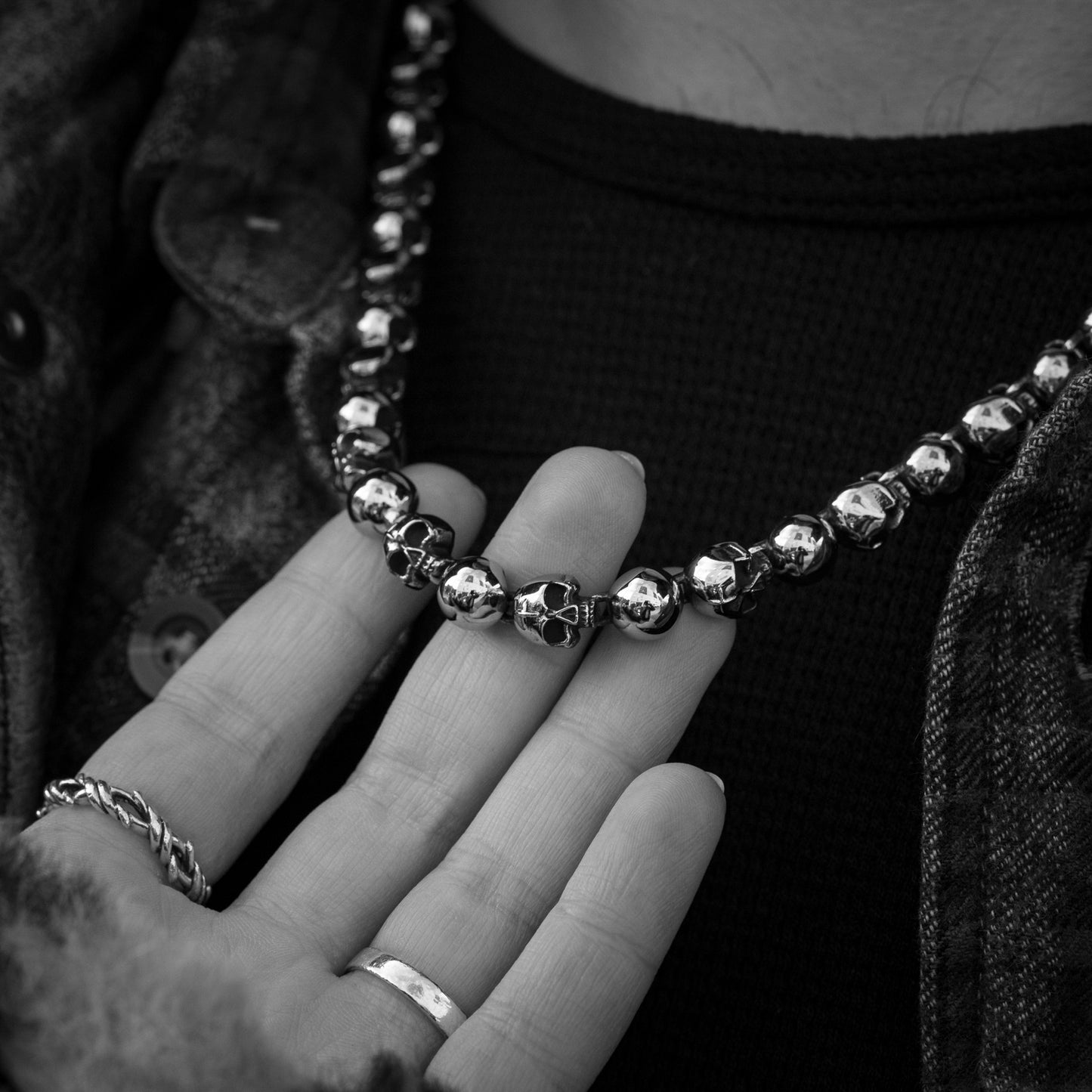 Close-up of a hand wearing a silver beaded necklace and ring.