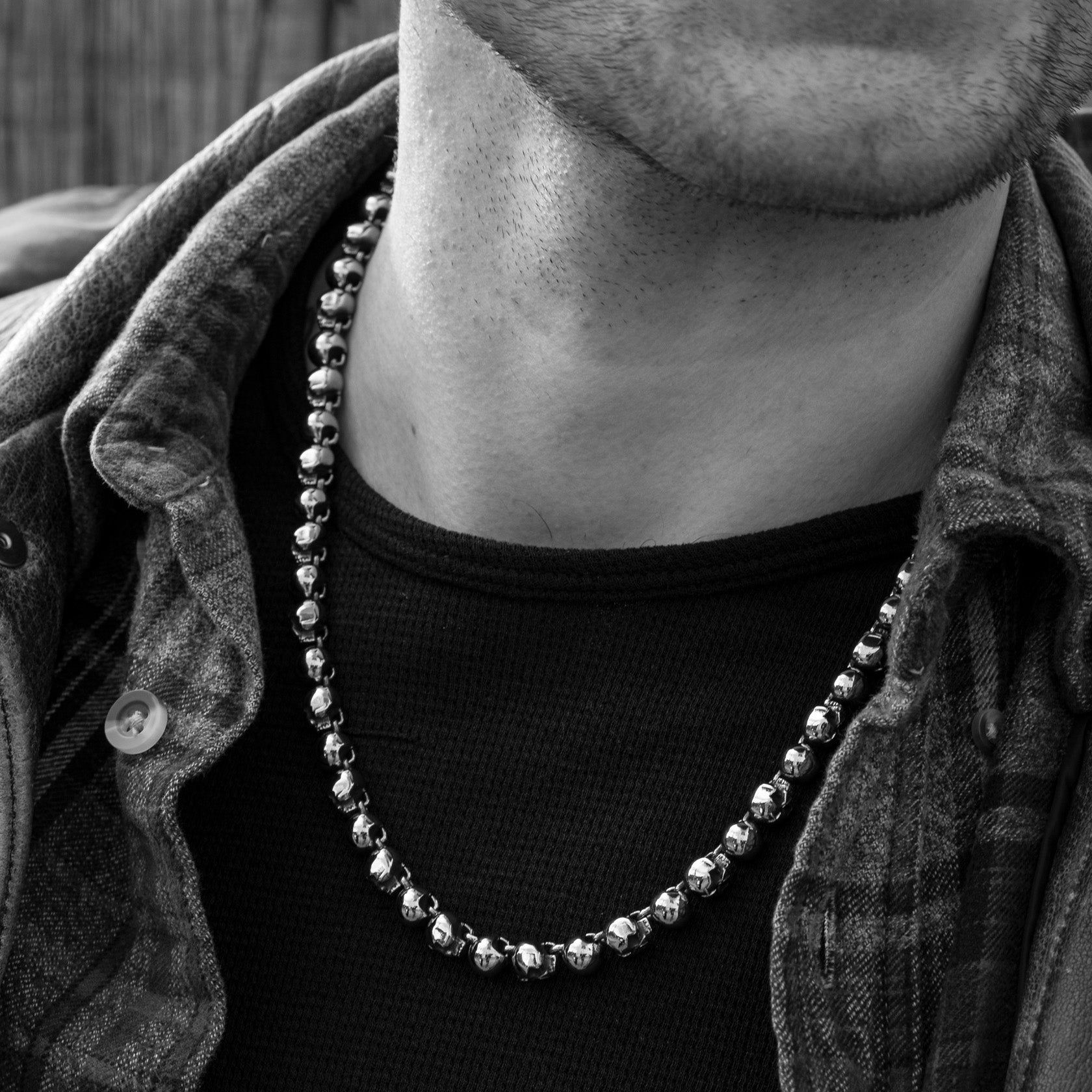 Person wearing a beaded necklace with a dark shirt and textured jacket.