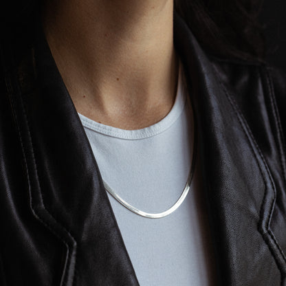 Silver herringbone chain necklace worn around person's neck over white shirt.