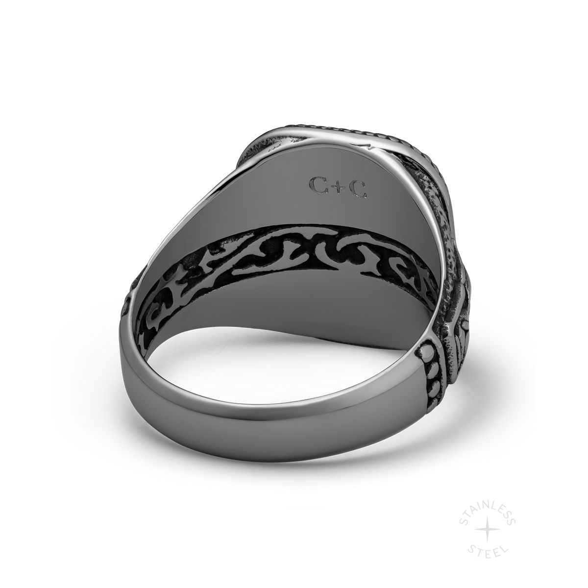 Stainless steel ring with ornate black patterned band and engraved top surface, shown from side angle.