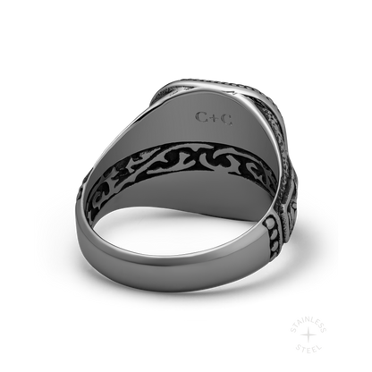 Stainless steel ring with ornate black patterned band and engraved top surface, shown from side angle.