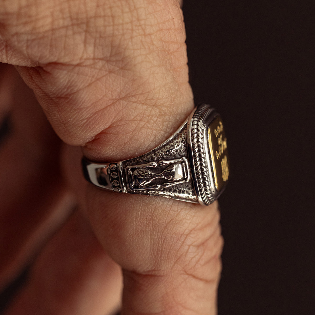 Silver and gold ornate signet ring with detailed engraving worn on finger.
