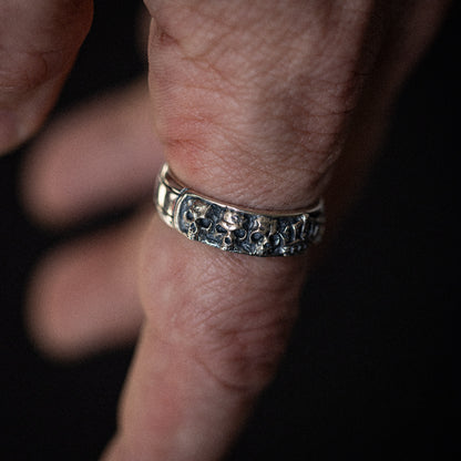 Silver textured band ring worn on a person's wrist against dark background.