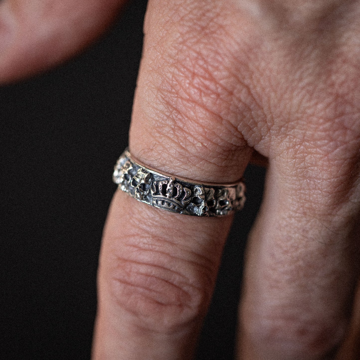 Silver ring with ornate embossed pattern worn on finger against dark background.