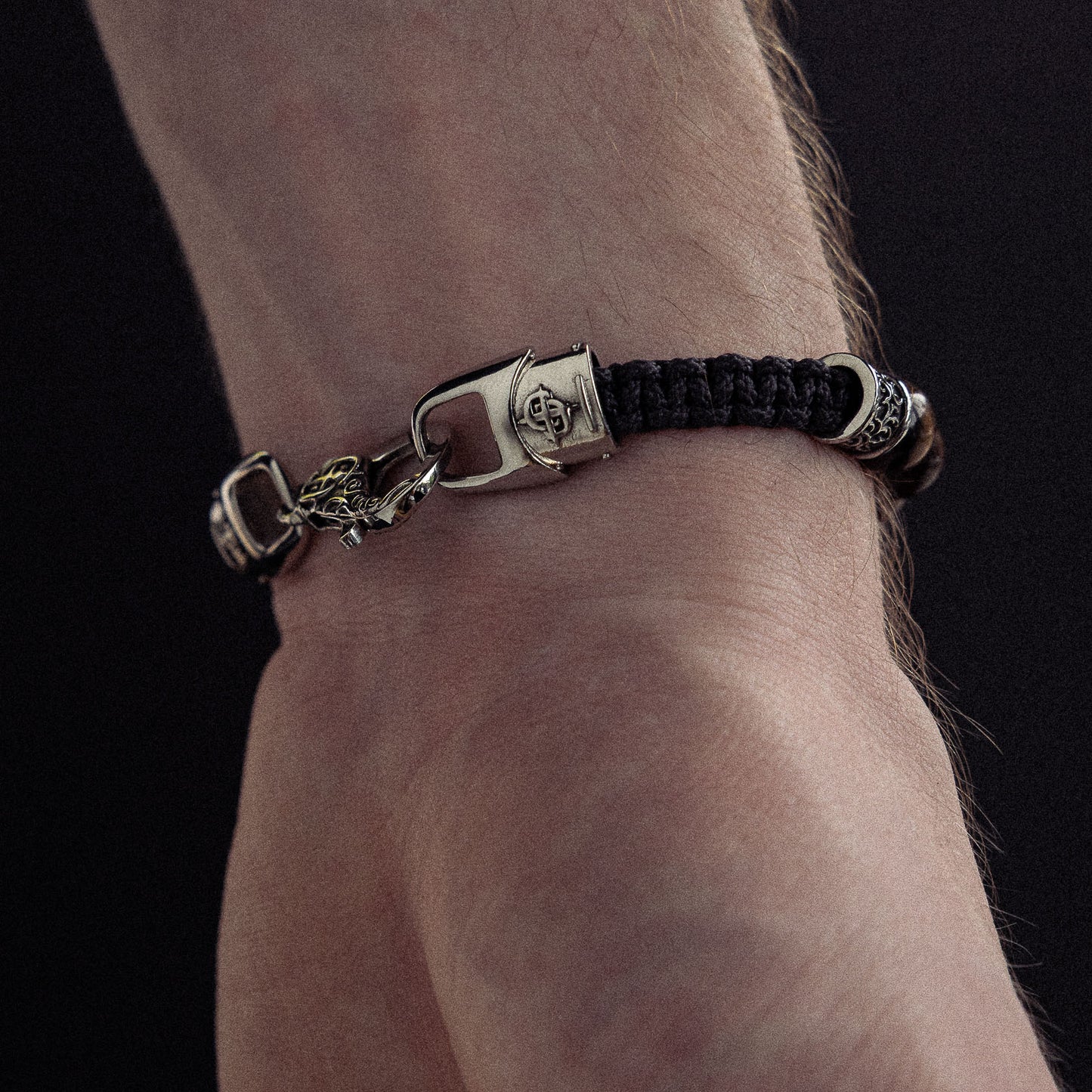 Bracelet with black woven cord, silver-tone metal clasp and charms worn on wrist.