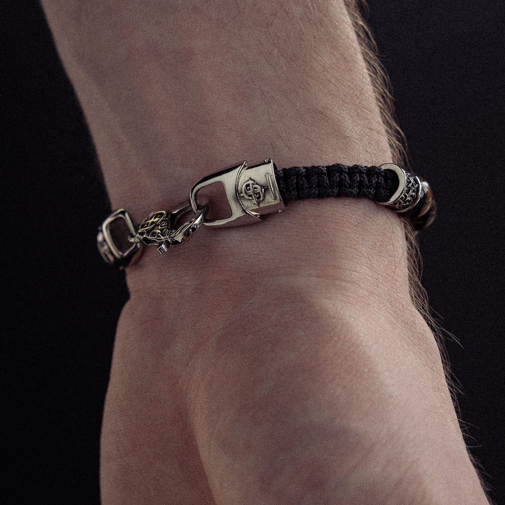Bracelet with black woven cord, silver-tone metal clasp and charms worn on wrist.