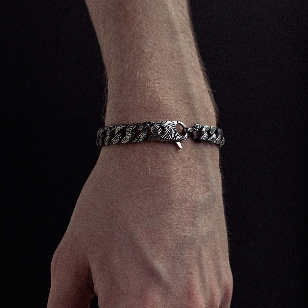 Silver-toned twisted chain bracelet with decorative clasp worn on wrist against dark background.