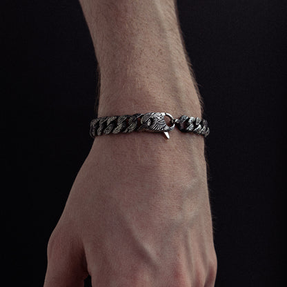 Silver-toned twisted chain bracelet with decorative clasp worn on wrist against dark background.